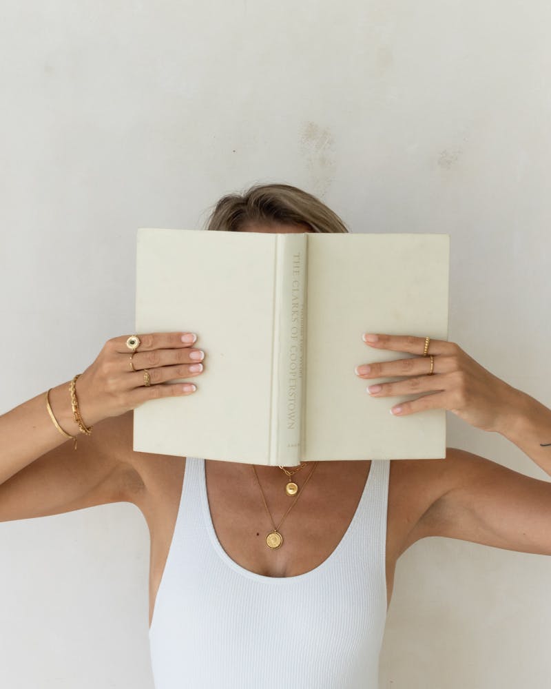 Woman holding book in front of her face with sustainable jewelry